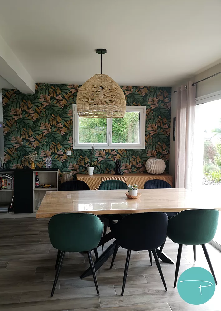 Salon, salle à manger et entrée à la décoration au style bohème chaleureux, cosy et coloré avec papier peint naturel vert, terracotta et jaune ocre. Murs vert dans salon et jaune ocre dans l'entrée. Mobilier en bois, suspension et lampadaire en fibre naturelle et chaises velours noir et vert